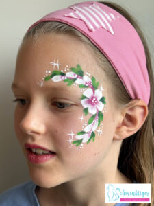 Kind geschminkt mit Blumenmotiv auf der Schläfe